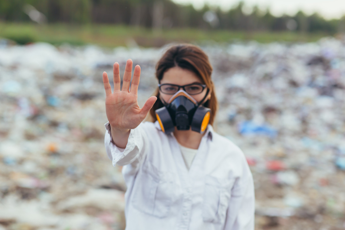 Woman wearing mask at landfill site with hand raised